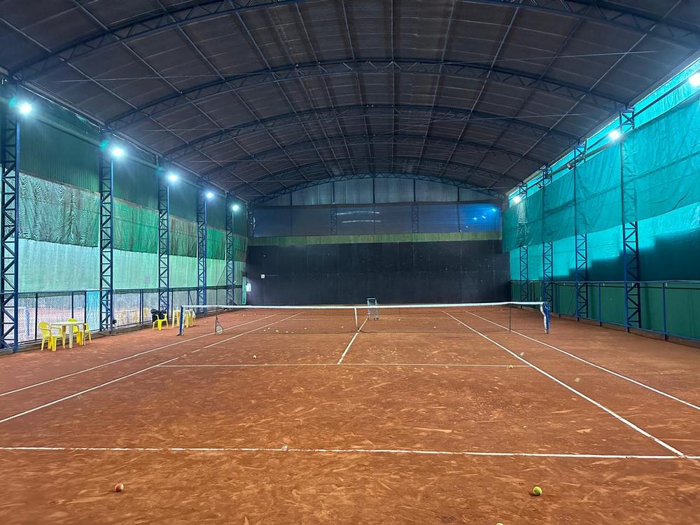 Quadra de saibro coberta, iluminada, com bolas espalhadas